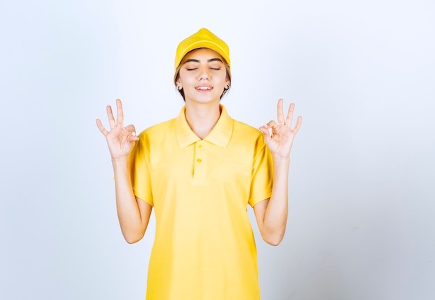 Lieferfrau in gelber Uniform, die steht und meditiert.