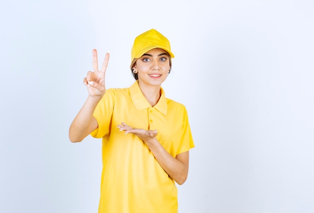 Lieferfrau in gelber Uniform, die zwei Finger zeigt und Victory-Zeichen macht.