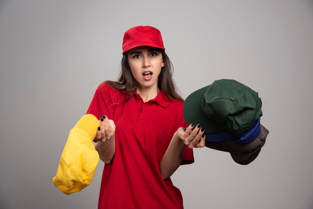 Lieferfrau mit bunten Kappen, die auf grauer Wand aufwerfen.