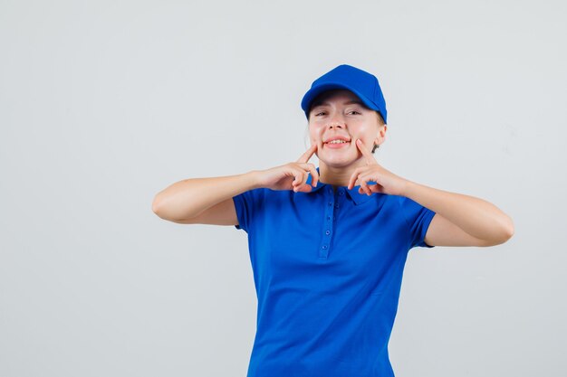 Lieferfrau zeigt auf ihre Grübchen in blauem T-Shirt und Mütze und sieht fröhlich aus