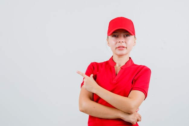 Lieferfrau zeigt zur Seite in rotem T-Shirt und Mütze und sieht zuversichtlich aus