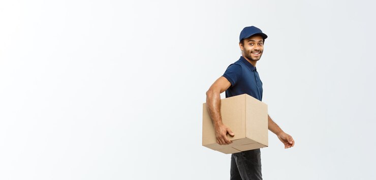 Kostenlose Foto lieferkonzept porträt eines glücklichen afroamerikanischen liefermanns in blauem tuch, der zu fuß geht, um ein kartonpaket an den kunden zu senden, isoliert auf grauem studiohintergrund, kopierraum