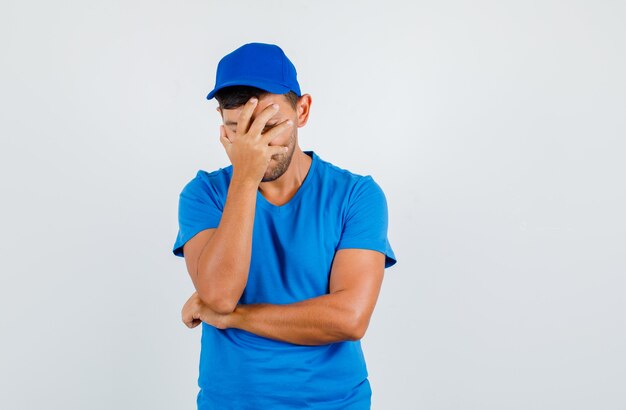 Liefermann, der Gesicht mit Hand im blauen T-Shirt, in der Kappe bedeckt und nachdenklich schaut.