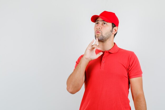 Liefermann, der mit Finger auf Kinn im roten T-Shirt nach oben schaut