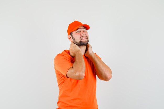 Liefermann leidet unter Nackenschmerzen in orangefarbenem T-Shirt, Mütze und sieht müde aus. Vorderansicht.