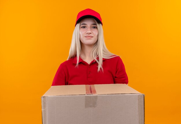 Lieferung junge Frau, die rotes T-Shirt und Kappe hält, die große Box auf isolierter orange Wand hält