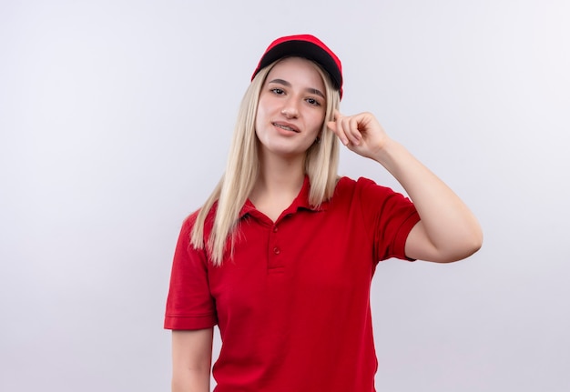 Lieferung junge Frau, die rotes T-Shirt und Kappe in Zahnspange trägt, legte ihren Finger auf Kopf auf isolierte weiße Wand