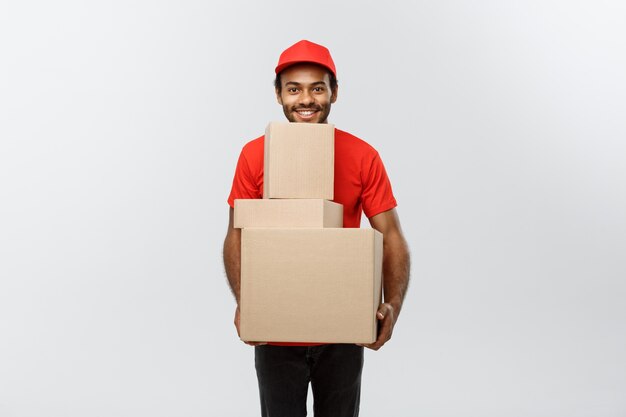 Lieferung Konzept - Porträt von Happy African American Lieferung Mann in rotem Tuch mit einem Box-Paket. Isoliert auf grau studio Hintergrund. Text kopieren