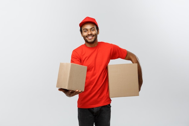 Lieferung Konzept - Porträt von Happy African American Lieferung Mann in rotem Tuch mit einem Box-Paket. Isoliert auf grau studio Hintergrund. Text kopieren