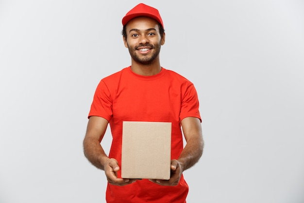 Lieferung Konzept - Porträt von Happy African American Lieferung Mann in rotem Tuch mit einem Box-Paket. Isoliert auf grau studio Hintergrund. Text kopieren