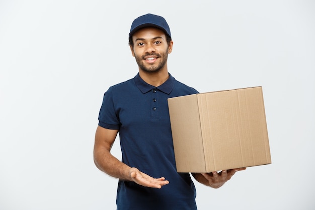 Lieferung Konzept - Porträt von Happy African American Lieferung Mann in rotem Tuch mit einem Box-Paket. Isoliert auf grau studio Hintergrund. Text kopieren