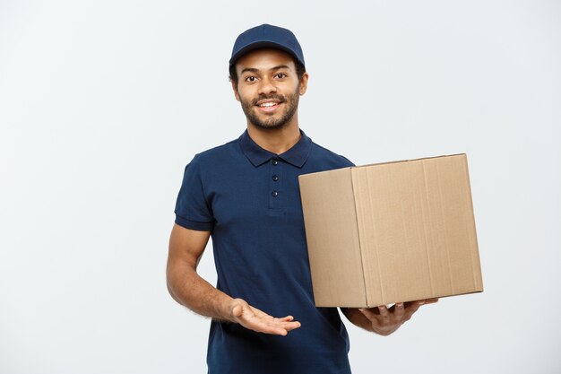 Lieferung Konzept - Porträt von Happy African American Lieferung Mann in rotem Tuch mit einem Box-Paket. Isoliert auf grau studio Hintergrund. Text kopieren