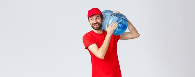 Lieferung von Speisen und Lebensmitteln zum Mitnehmen covid19 Konzept für kontaktlose Bestellungen Fröhlich lächelnder bärtiger Kurier in roter Uniformkappe bringt Wasser in Flaschen ins Büro oder Haus und schaut freudig weg