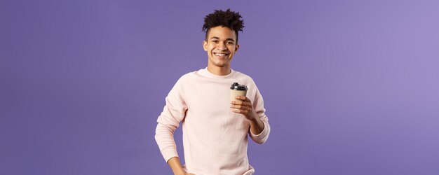 Lifestyle Café Eatingout Konzept Porträt eines fröhlichen jungen hispanischen Kerls, der eine Tasse Cof zum Mitnehmen hält