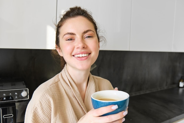 Lifestyle-Konzeptporträt einer glücklichen brünetten Frau im Bademantel, die in der Küche Kaffee trinkt