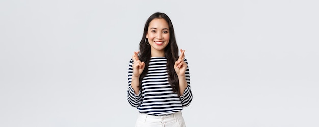 Lifestyle-Menschen Emotionen und lässiges Konzept Hoffnungsvolle, aufgeregte, süße koreanische Frau, die sich mit gekreuzten Fingern lächelnd wünscht, in Erwartung positiver Nachrichten, die plädieren, dass ein Traum wahr wird