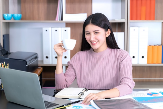 Lifestyle schöne asiatische Business junge Frau am Schreibtisch heiße Kaffeetasse an Hand