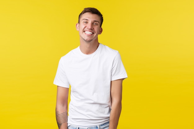 Lifestyle, sommer und menschen emotionen konzept. hübscher charismatischer kaukasier im lässigen weißen t-shirt, das breit mit perfektem weißem lächeln lächelt und fröhlichen gelben hintergrund steht.