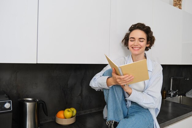 Lifestyle- und People-Konzept. Eine junge Frau genießt das Wochenende zu Hause und liest Notizen in ihrem Tagebuch