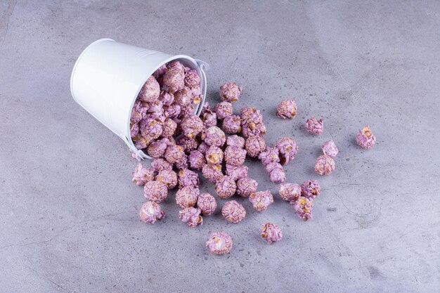 Lila kandiertes Popcorn, das aus einem Eimer auf Marmorhintergrund gießt. Foto in hoher Qualität