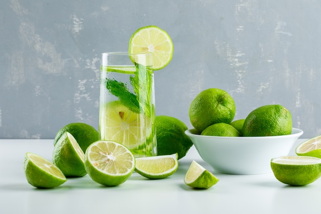 Limonade in einem Glas mit Zitronen, Kräuterseitenansicht auf Weiß und Gips