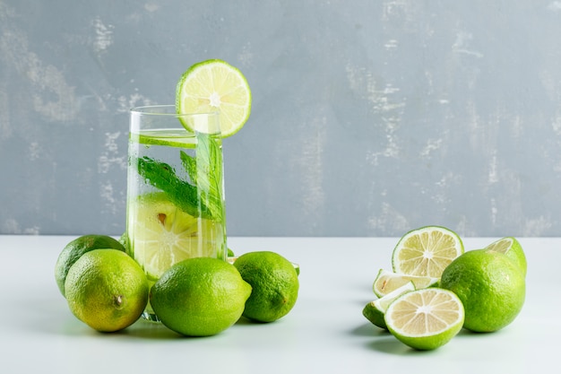 Limonade in einem Glas mit Zitronen, Kräuterseitenansicht auf Weiß und Gips