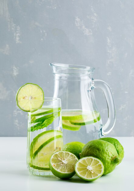 Limonade in Glas und Krug mit Zitrone, Basilikum Seitenansicht auf Weiß und Gips