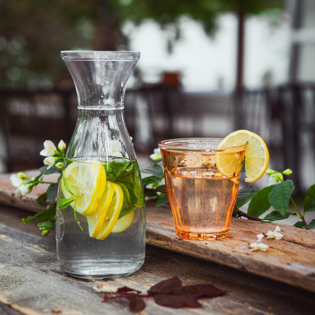 Limonade mit Blumen auf Zweig in Glas und Krug auf Holz und Hof Tisch, Seitenansicht.