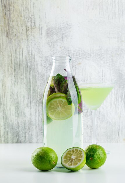 Limonade mit Zitronen, Basilikum in Flasche und Glas auf weiß und grungy,