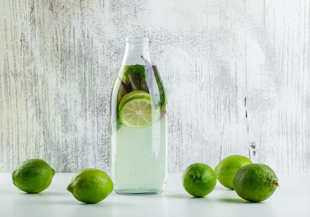 Limonade mit Zitronen, Basilikumblätter in einer Flasche auf weiß und grungy,