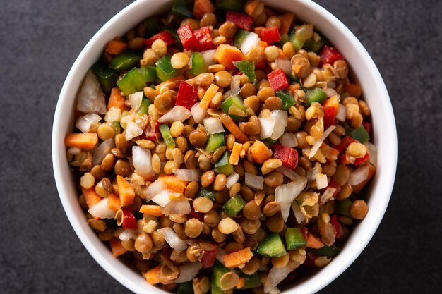 Linsensalat mit Peppersonion und Karotte in einer Schüssel auf schwarzem Schieferhintergrund