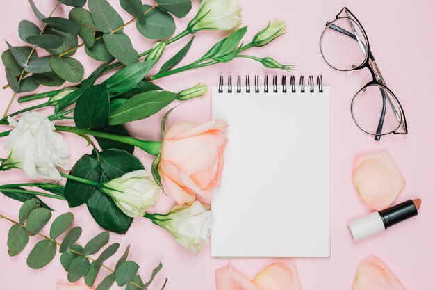 Lippenstift; Brille; rosafarbener Rosen- und Eustomablumenblumenstrauß über rosa Hintergrund