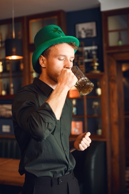 Kostenloses Foto lockiger mann in einem grünen hut. guy trinkt bier. mann feiert einen feiertag in einer kneipe.