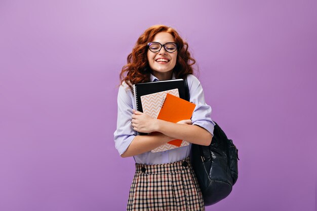 Lockiges Mädchen mit Brille hält Notizbücher an lila Wand