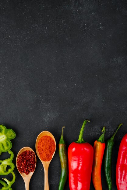 Löffel Gewürze und Paprika auf schwarzem Tisch