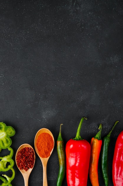 Löffel Gewürze und Paprika auf schwarzem Tisch