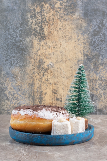 Lokums, Donut und eine Baumfigur auf einer blauen Platte auf Marmor.