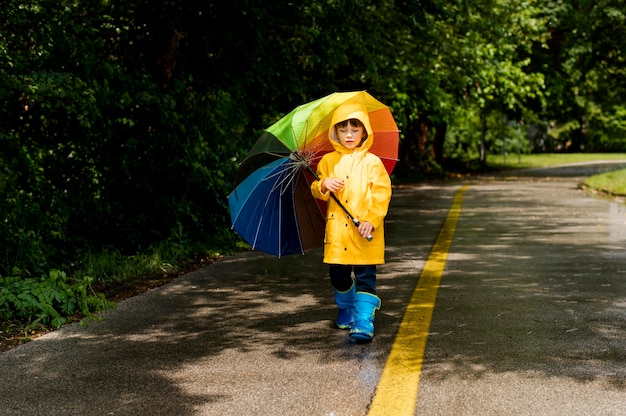 Kostenloses Foto long shot kleiner junge hält einen regenschirm über dem kopf