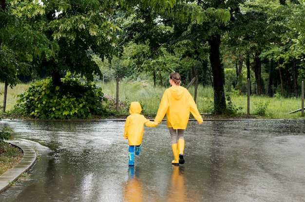 Long Shot Mutter und Sohn Händchen haltend beim Tragen von Regenmänteln