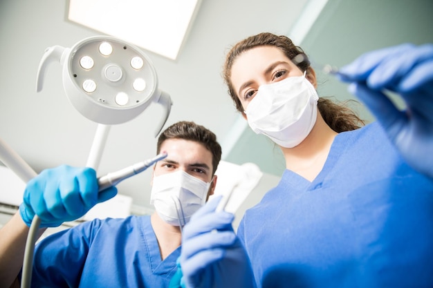 Low Angle Portrait von männlichen und weiblichen Zahnärzten, die Masken tragen, während sie in der Zahnklinik arbeiten