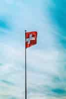 Kostenloses Foto low angle shot der schweiz flagge auf einer stange unter dem atemberaubenden bewölkten himmel