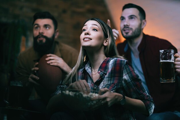 Low Angle View von Sportfans, die zu Hause ein Spiel im Fernsehen ansehen Der Fokus liegt auf der Frau mit Popcorn
