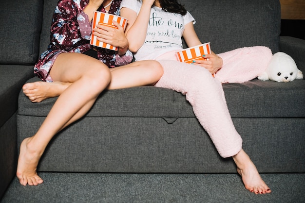 Kostenloses Foto lowsection-ansicht von zwei frauen, die auf sofa mit popcorn sitzen