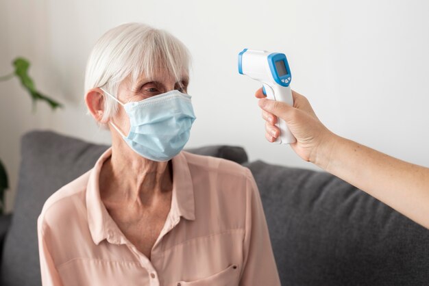 Ältere Frau, deren Temperatur mit Thermometer überprüft wird