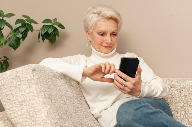 Ältere Frau des hohen Winkels auf Couch unter Verwendung des Telefons