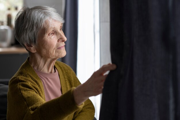 Ältere Frau des mittleren Schusses, die aus dem Fenster schaut