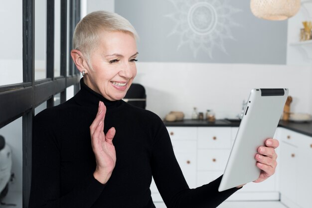 Ältere Frau des smiley in der Küche, die an der Tablette wellenartig bewegt