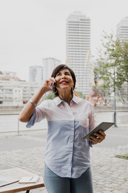 Ältere Frau, die am Telefon auf städtischem Hintergrund spricht