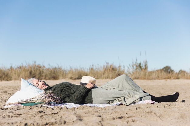 Ältere Frau, die auf Sand liegt