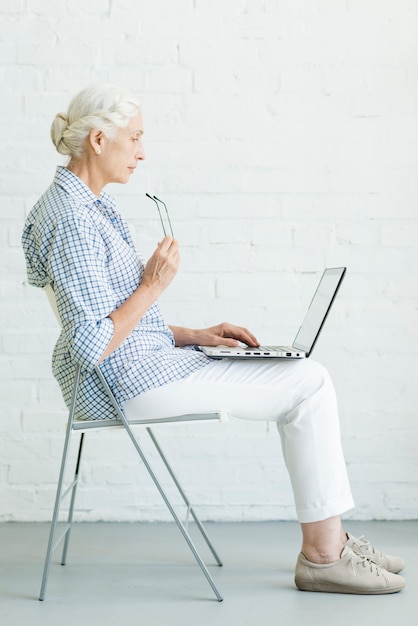 Ältere Frau, die auf Stuhl unter Verwendung des Laptops sitzt